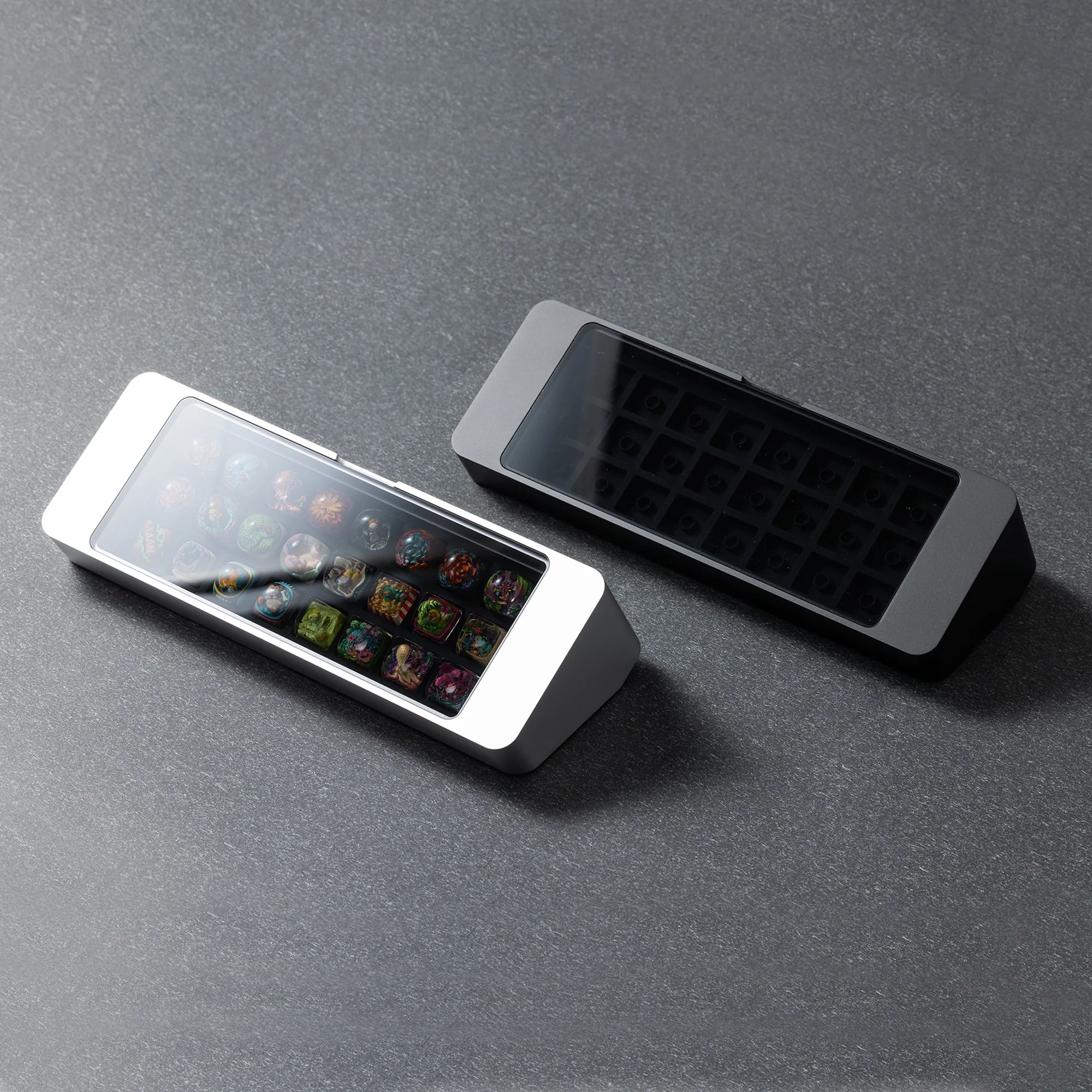 Bliss Artisan Tray shown in Black and Silver finishes — 24-slot keycap display case with tempered glass lid