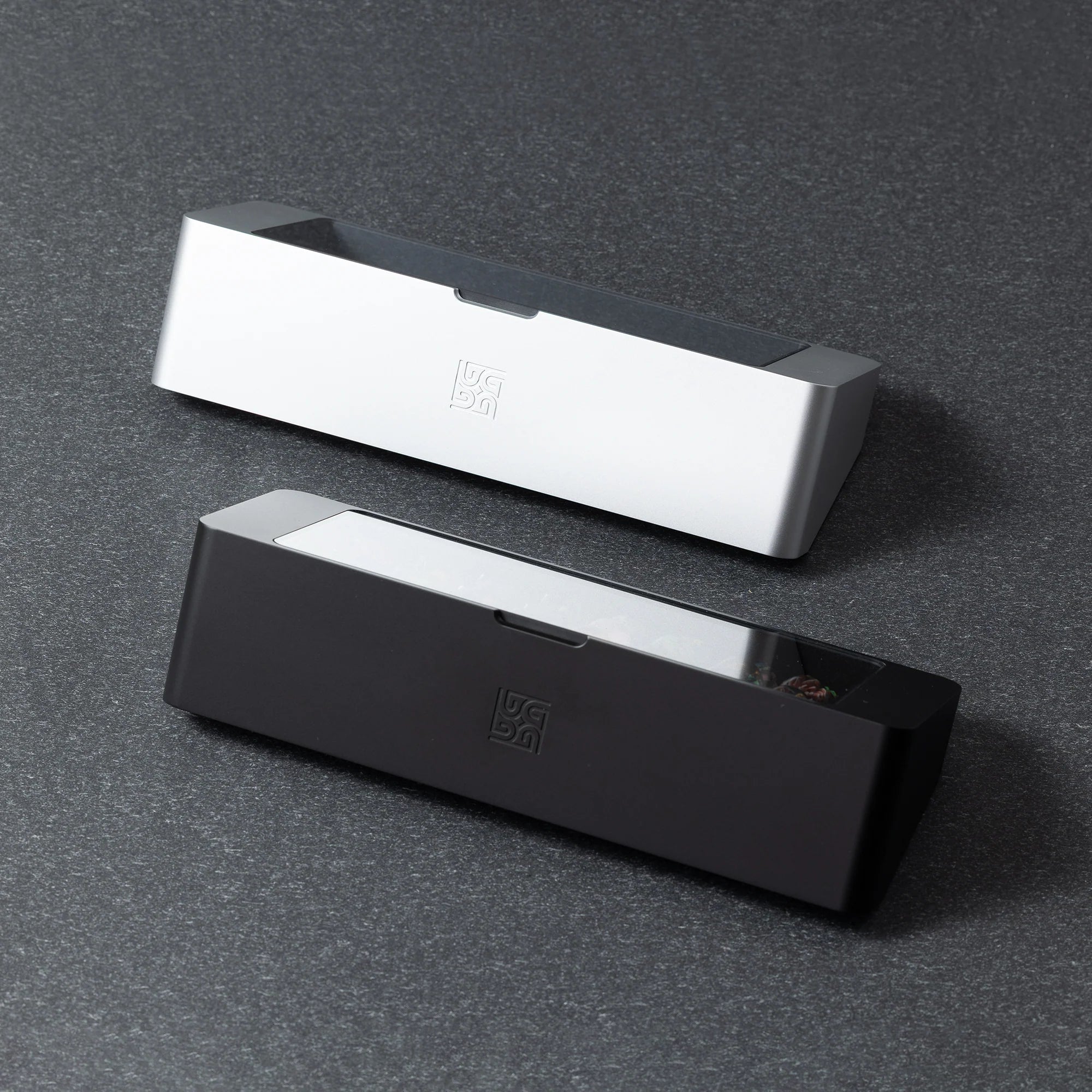 Bliss Artisan Tray shown in Black and Silver finishes — 24-slot keycap display case with tempered glass lid